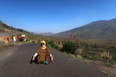 Full length of man sitting on road against clear blue sky