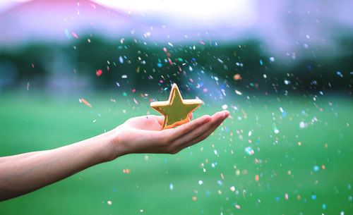 Cropped hand of woman holding golden star shape with confetti in mid-air