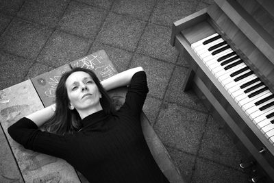 High angle view of thoughtful woman lying down by piano on table