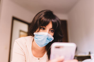 Low angle view of young woman using mobile phone while lying at home