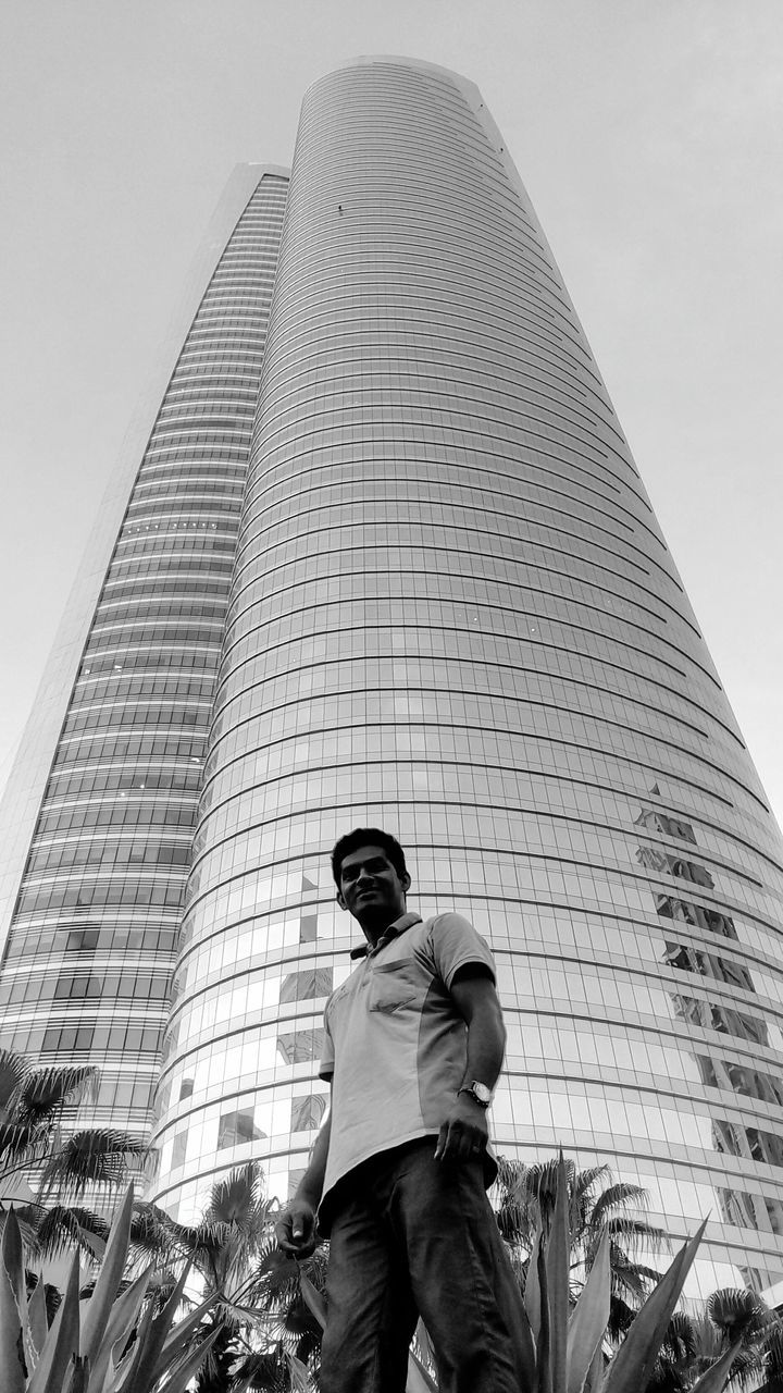 low angle view, architecture, built structure, building exterior, one person, real people, modern, city, skyscraper, lifestyles, standing, outdoors, day, young adult, men, sky, adult, people, adults only