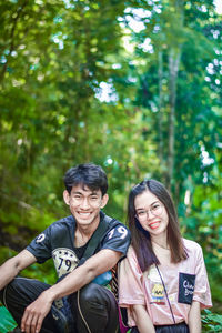 Portrait of smiling young couple sitting against trees