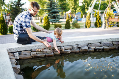 Man looking at daughter playing with water in fountain at park