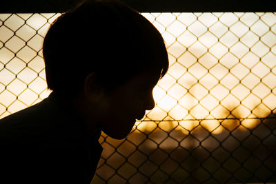 Silhouette of boy against wired fence