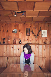 Beautiful young woman sitting at home against wooden wall