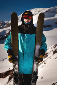 Skier confident sports man in goggles mask, spends extreme weekend in the mountains, holds skis next