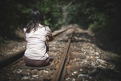 Rear view of woman sitting on railroad track