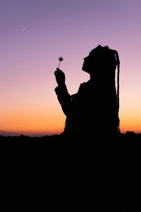 Silhouette woman holding lollipop standing against sky during sunset