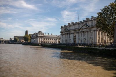 Buildings by river against cloudy sky