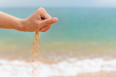 Close-up of a woman's hand releasing falling sand. sand flows through the hand against the backdrop