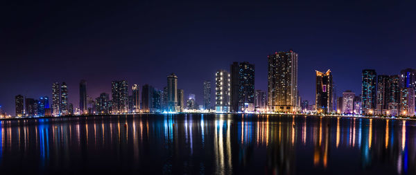 Illuminated buildings by river against sky at night