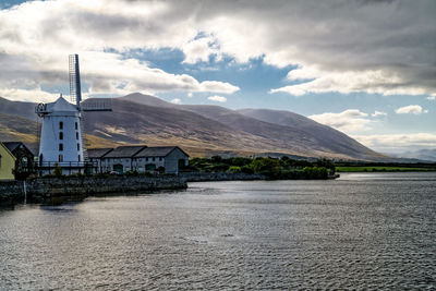 Traditional windmill by lake against sky