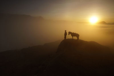 Silhouette man and horse on mountain cliff