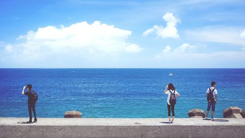 Tourist standing on retaining wall of sea against cloudy sky