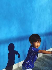 Cheerful boy standing against blue wall