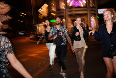 Group of stylish multiracial friends walking together on city street for party at night