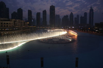 Illuminated buildings by river against sky in city at night