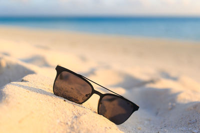 Close-up of sunglasses on sand at beach against sky