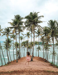 Rear view of woman running against palm trees at beach against sky