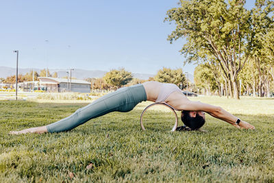 Fit young woman practicing yoga in the park. stretching on the wheel