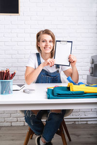 Portrait of smiling young woman using phone while sitting on table