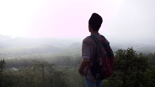 Rear view of man standing on mountain against clear sky