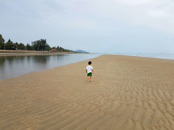 Boy walking at beach against sky