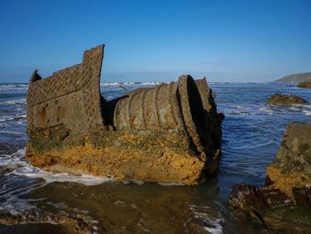 Shipwreck boiler on beach against clear sky