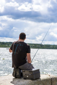 Rear view of man fishing at a lake against sky