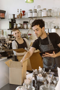 Male owner checking inventory with female colleague holding box in background
