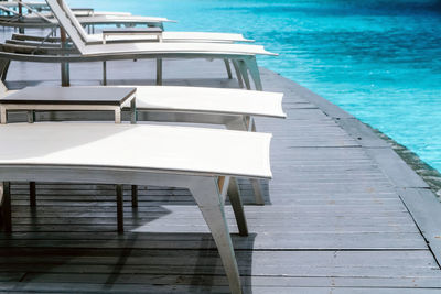 Empty chairs by swimming pool against sea