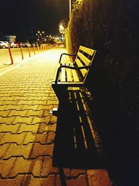 Empty bench on footpath in city at night