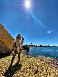 Side view of woman standing by lake against sky