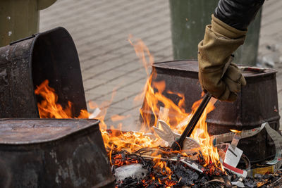 A cropped hand wearing fire resistant gloves places raku ware into a reduction fire tongs