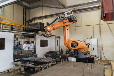 Business people standing by automatic robot arm machine at factory