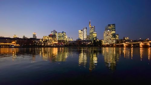 Illuminated buildings by river against sky