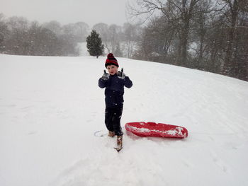 Full length of boy showing thumbs up on snow covered field