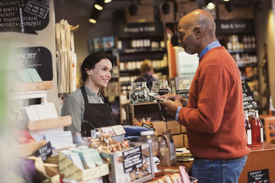 Smiling owner talking to customer holding packet while standing at store