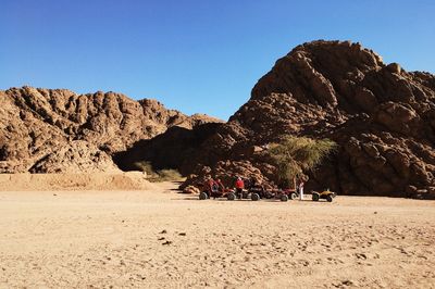 People on rock formations in desert against clear sky