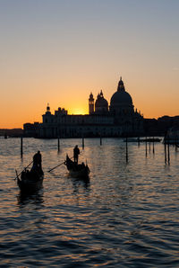 Gondoliers sailing on grand canal against santa maria della salute during sunset