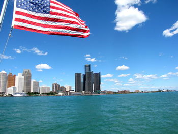 American flag by detroit river against sky in city