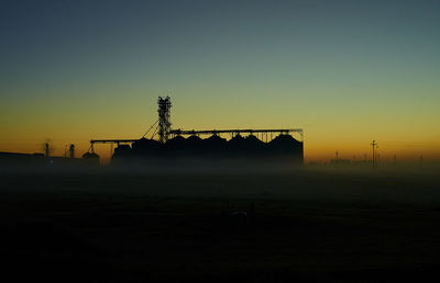 Silhouette cranes on field against clear sky at sunset