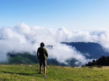 Rear view of man standing on mountain against cloudy sky