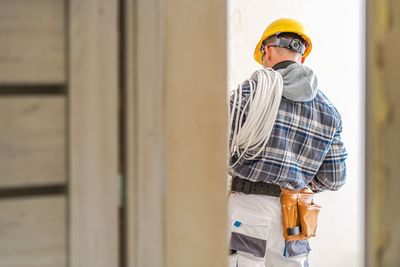 Rear view of electrician wearing hardhat with cables standing against wall