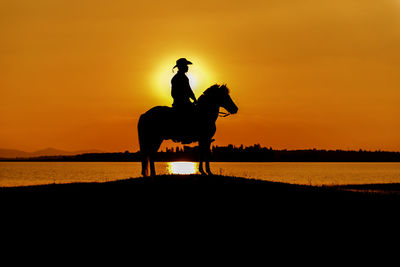 Silhouette man riding horse at sunset