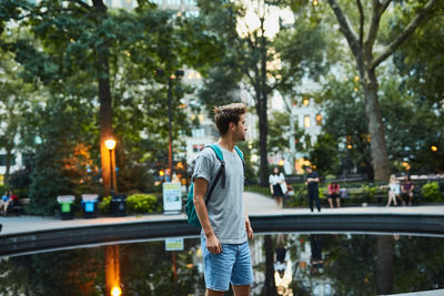 Young man standing by pond in city