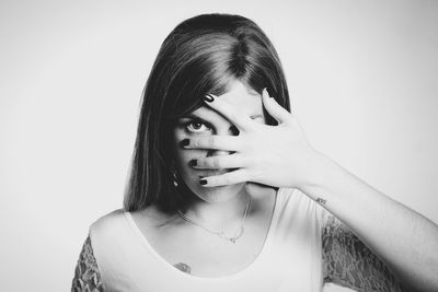 Close-up portrait of young woman covering face against white background