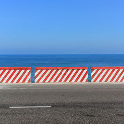 Striped retaining wall on road by sea against clear sky