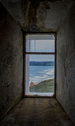 Sea against cloudy sky seen through window