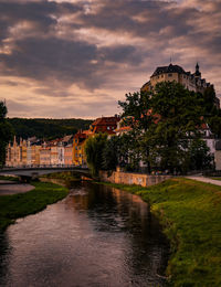 River amidst buildings and castle against sky during sunset